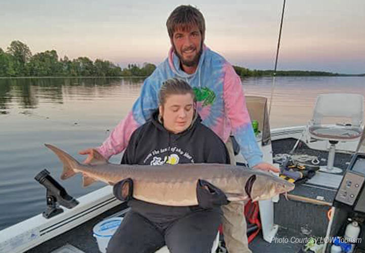 image on young woman holding big sturgeon caught on the rainy river