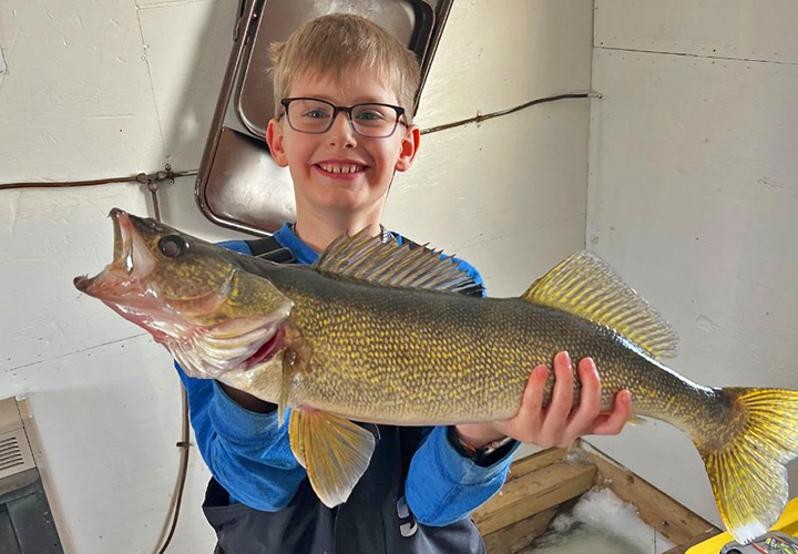 image of young ice fisherman holding big walleye caught on Lake of the Woods